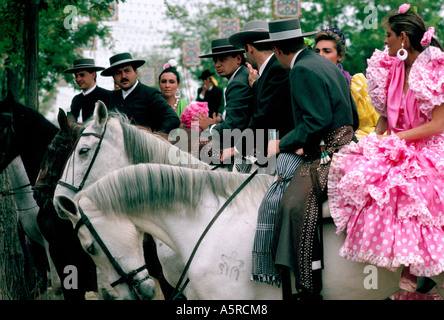 Gli uomini indossando il tradizionale abito grigio donne abbigliate IN SAVILLANAS costume di flamenco a cavallo di due fino a cavallo presso la fiera di Siviglia Foto Stock