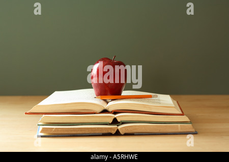 Pila di aprire i libri di scuola, rosso apple e matita su scrivania con lavagna in background. Foto Stock