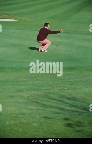 Il Golfer accovacciato sul verde, tenendo fuori pugno Foto Stock