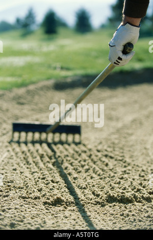 Il Golfer rastrellando sabbia nella trappola di sabbia Foto Stock