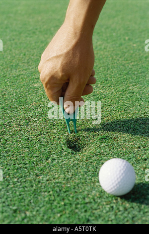 Il Golfer foro utilizzando lo strumento di riparazione sul tappeto erboso, close-up di mano Foto Stock