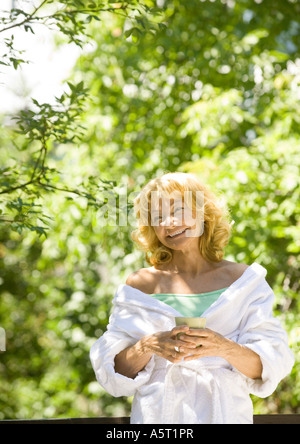 Senior donna che indossa accappatoio, tenendo mug, all'aperto Foto Stock