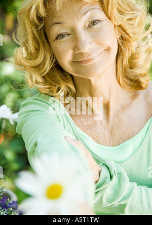 Senior donna tenendo fuori fiore, ritratto Foto Stock