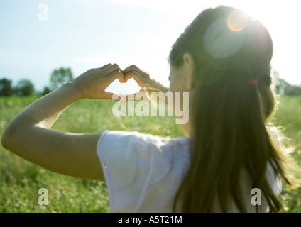 Ragazza nel campo, rendendo forma di cuore con le mani, vista posteriore Foto Stock