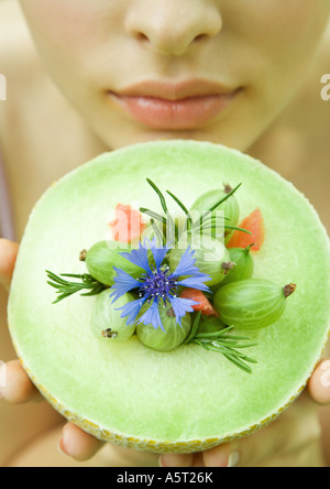 Donna che mantiene fino di melone Honeydew rabboccato con bacche, fiori e rametti di rosmarino, close-up Foto Stock