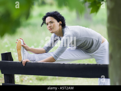 Giovane donna stretching gamba sulla recinzione di legno Foto Stock