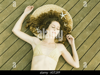 Donna in bikini giacente sul ponte, stelle marine nei capelli, occhi chiusi Foto Stock