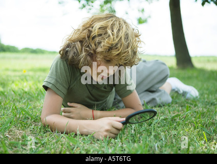 Ragazzo che giace in erba con lente di ingrandimento Foto Stock