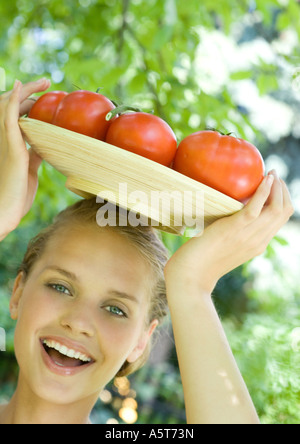 Donna che mantiene ciotola piena di pomodori sulla parte superiore della testa Foto Stock