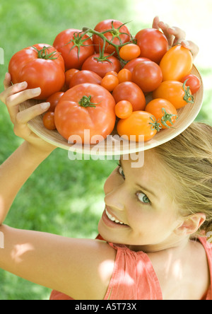 Donna che mantiene ciotola piena di pomodori sulla parte superiore della testa Foto Stock