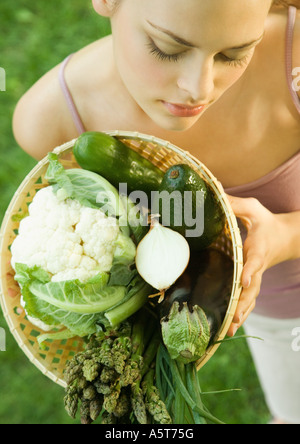 Giovane donna mantenendo la cesta piena di verdure Foto Stock