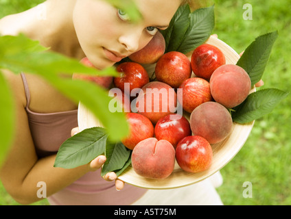 Giovane donna mantenendo la ciotola di pesche e pesche noci Foto Stock