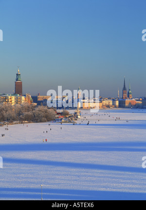 La gente camminare attraverso mezzo di Stoccolma in inverno a Riddarfjarden congelato per via navigabile con il Municipio sulla sinistra Foto Stock
