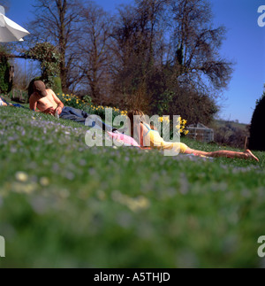 Gli adolescenti sdraiati sull'erba in un giardino di campagna con i narcisi in aprile a prendere il sole e la lettura di libri in Wales UK KATHY DEWITT Foto Stock