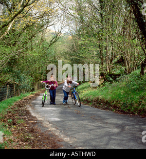 Due giovani ragazze spingendo le bici fino alla cima di una collina su un vicolo del paese in Carmarthenshire Wales UK KATHY DEWITT Foto Stock