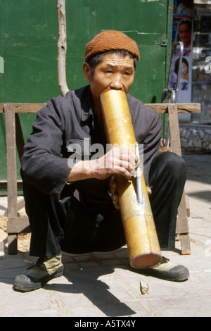 Uomo locale nei tradizionali giacca blu di fumare una sigaretta attraverso un grande tubo di bambù sulla strada kunming nella provincia dello Yunnan in Cina Foto Stock