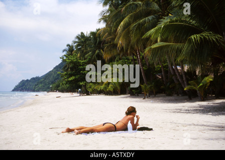 Slim western turista femminile sunbathes su una spiaggia deserta orlata di palme,Koh Chang,della Thailandia. Foto Stock