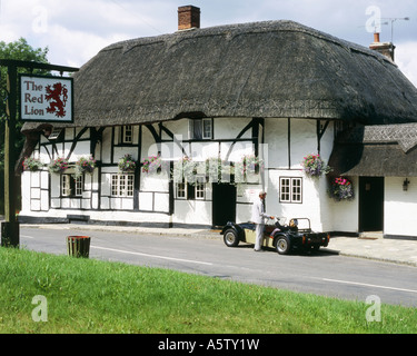 L'uomo aiutando la donna al di fuori della vettura sportiva di fronte alla vecchia,con il tetto di paglia, Pub Red Lion,Chalton hampshire,U.K. Foto Stock