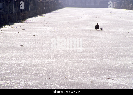 Uomo locale si siede da solo la pesca su un fiume congelato di ghiaccio dalla città proibita,Beijing, Cina. Foto Stock