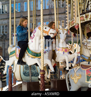 Due bambine rotonda di equitazione cavalli in legno Foto Stock