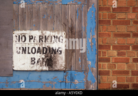 Logoro e sporco avviso su un peeling blu porta di legno in una parete di mattoni con il messaggio Nessun parcheggio alloggiamento di scarico Foto Stock