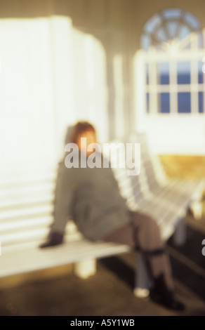 Impressionistica figura avvolto in abiti invernali, seduto su un banco di bianco in un bianco rifugio e godersi il sole Foto Stock