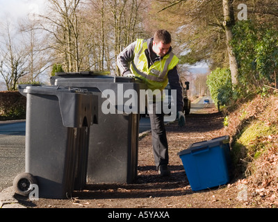 L'uomo la raccolta dal marciapiede re-cycling caselle accanto a 2 scomparti wheelie di rifiuti domestici su strada su bin giorno di raccolta. Scozia UK Foto Stock