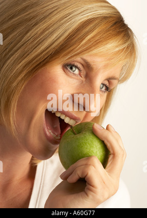 Attraente giovane donna bionda di mordere in Fresca mela verde Foto Stock