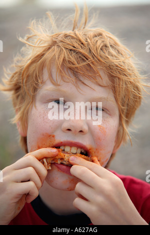 Ritratto di una giovane dai capelli rossi boy con lentiggini mangiare una ala di pollo Foto Stock