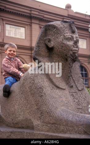 Giovane ragazzo bianco seduto su una sfinge nel giardino di sculture in ingresso al Museo Egizio delle Antichità Cairo Egitto Foto Stock