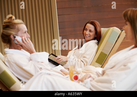 Profilo laterale di una donna matura a parlare su un telefono mobile con due metà donne adulte guardando lei Foto Stock