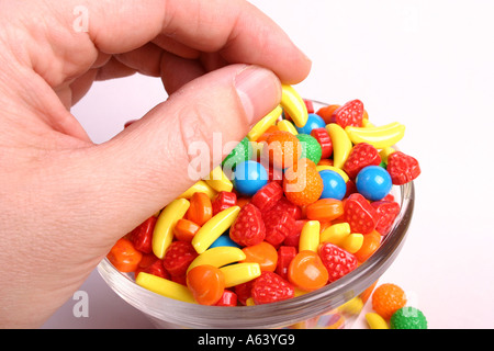 Caramelle in una ciotola con una chiusura su una mano tenendo caramelle Foto Stock