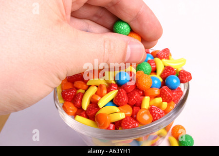 Caramelle in una ciotola con una chiusura su una mano tenendo caramelle Foto Stock