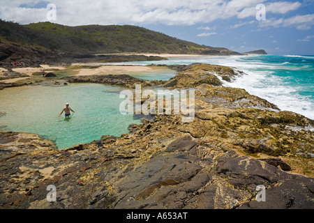 Un visitatore wades in una roccia naturale piscina fiancheggiante l'oceano su Fraser Island a nord di punta orientale Foto Stock