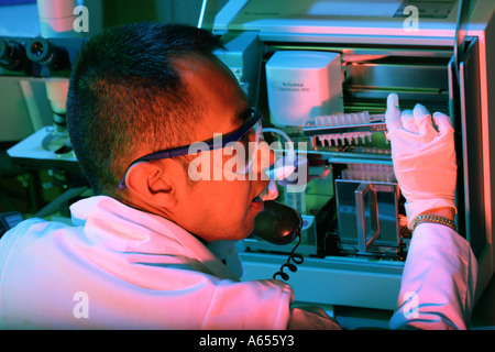 Asian ricercatore maschio utilizza la macchina di DNA e telefono. Controllo DNA forense. Foto Stock