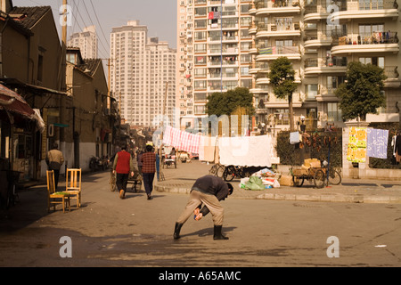 Shanghai, Cina. La città vecchia incontra il nuovo come un uomo fa il suo esercizio mattutino in strada la biancheria appesa ad asciugare Foto Stock