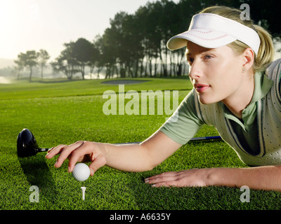 Giovani femmine golfista giacente sulla corte, ponendo la sfera sul raccordo a T Foto Stock