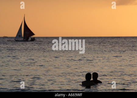 Barca a vela dietro una giovane coppia Filapino sulla loro abbraccio luna di miele sulla spiaggia di Boracay, Isole Filippine Foto Stock
