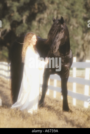Giovane donna in abito bianco con il nero il frisone stallone Foto Stock
