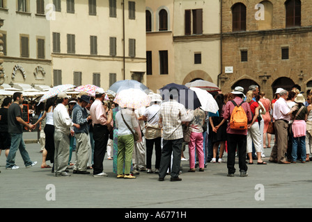 Firenze gruppo di turisti si riuniscono intorno alla guida in Piazza della Signoria il ricovero sotto gli ombrelloni in una calda giornata estiva Firenze Toscana Italia Foto Stock