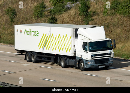 Vista laterale e frontale Waitrose supermercato business food supply chain negozio consegna camion e conducente rimorchio con logo e Royal warrant autostrada UK Foto Stock