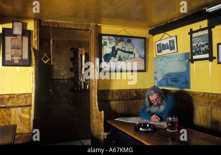 Pub Square e Compass, Ray Newman publican. Worth Matravers, Dorset. Fumare leggendo una pinta di birra di giornale sotto un ritratto di suo padre Charlie. Foto Stock