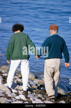 Una coppia senior tenere mani come essi passeggiare sulla riva Foto Stock
