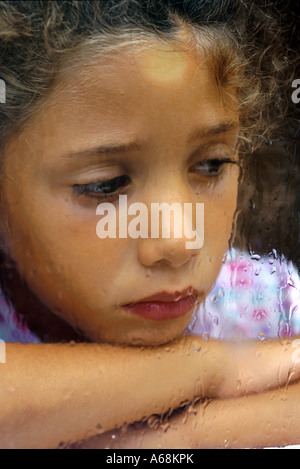 Ragazza triste guardando fuori la pioggia finestra con striature Foto Stock