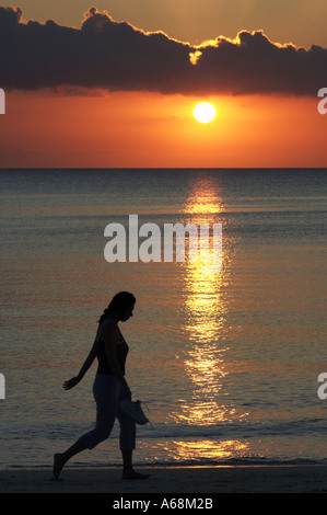 Donna che cammina sulla spiaggia al tramonto Foto Stock