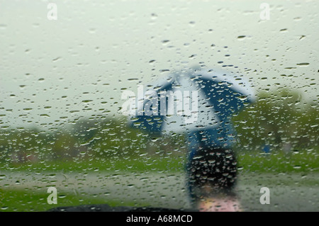 Vista di un pedone con un ombrello coloratissimo visto anche se le gocce di pioggia su di un parabrezza di automobile Foto Stock