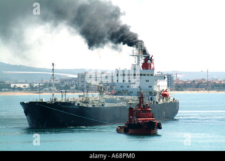 Emissioni di fuliggine e fumo nero che si estendono dall'imbuto della nave da carico inquinando l'atmosfera locale e l'ambiente che arriva al porto di Palma Mallorca Spagna e UE Foto Stock