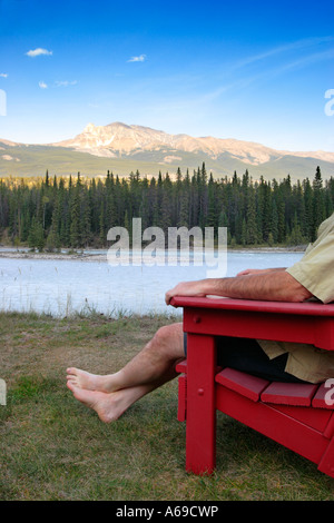 Uomo seduto in poltrona a sdraio affacciato sul fiume di montagna Foto Stock