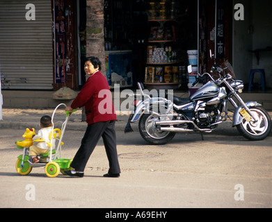 Nonna spingendo il suo nipote in un lussuoso baby buggy lungo una copia cinese di un American chopper. Jinghong, Yunnan. Cina. Foto Stock