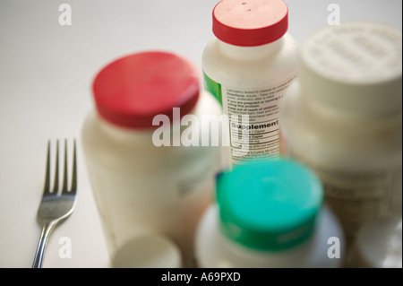 Studio shot di bottiglie di plastica di pillole e integratori alimentari con la lama di un coltello e forchetta su una superficie bianca 2006 Foto Stock